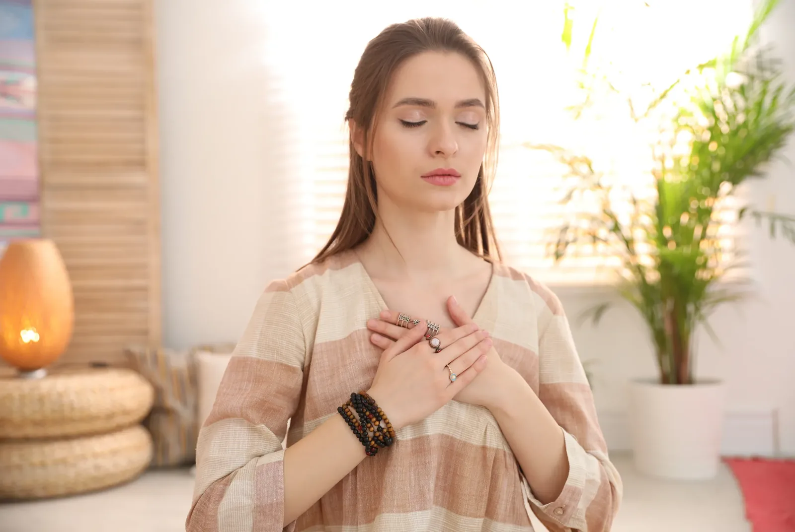 A woman sitting quietly with both hands resting on her chest, taking a reflective pause in a warmly lit room