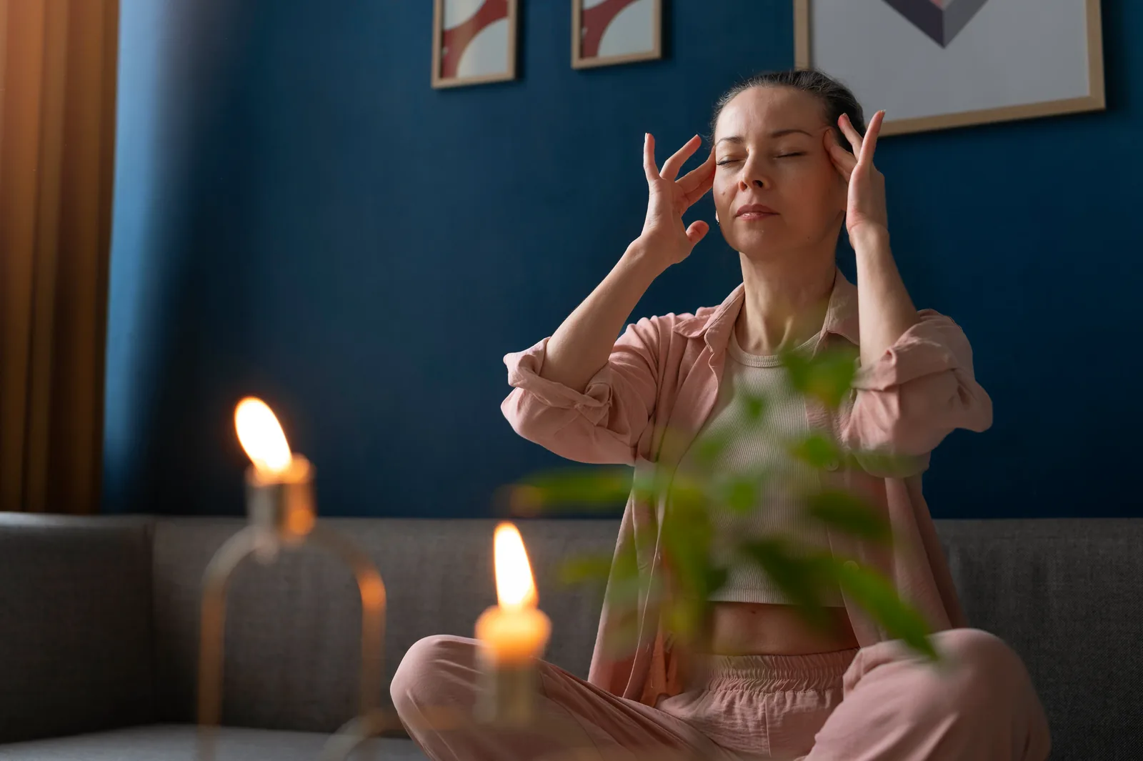 A woman seated in a calm meditative posture beside softly lit candles, taking time for quiet self-reflection